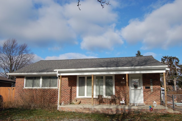 view of front of property with a shingled roof, fence, and brick siding