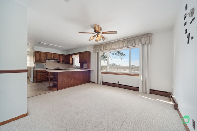 kitchen with light carpet, kitchen peninsula, ceiling fan, sink, and a breakfast bar area