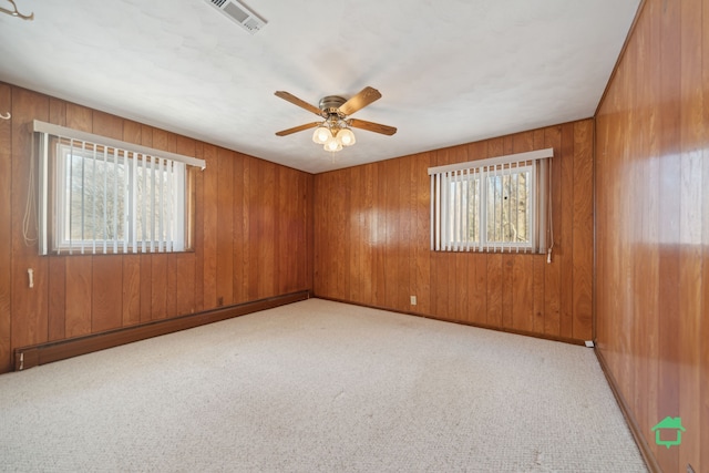 carpeted spare room with baseboard heating, wooden walls, plenty of natural light, and ceiling fan