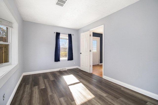 empty room with a textured ceiling, dark hardwood / wood-style flooring, and a wealth of natural light