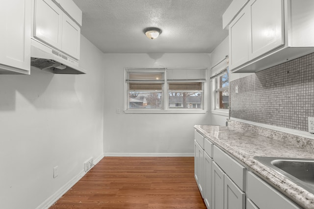 kitchen with sink, decorative backsplash, a textured ceiling, white cabinetry, and wood-type flooring