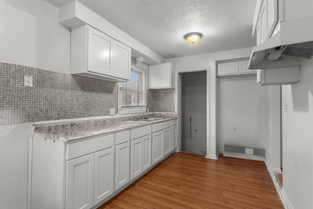 kitchen with backsplash, white cabinetry, a textured ceiling, and light wood-type flooring