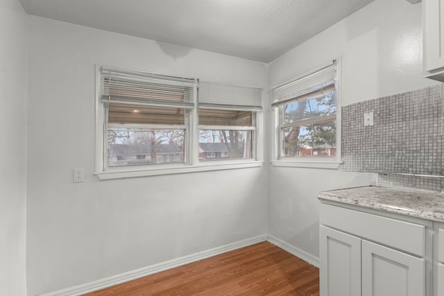 kitchen with white cabinets, tasteful backsplash, light hardwood / wood-style flooring, and light stone countertops