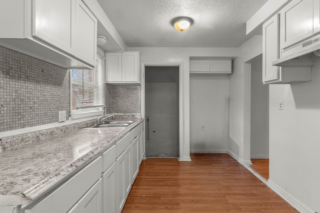 kitchen with light wood-type flooring, tasteful backsplash, a textured ceiling, sink, and white cabinets