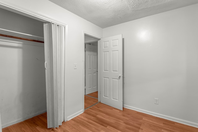 unfurnished bedroom with a textured ceiling, light hardwood / wood-style floors, and a closet