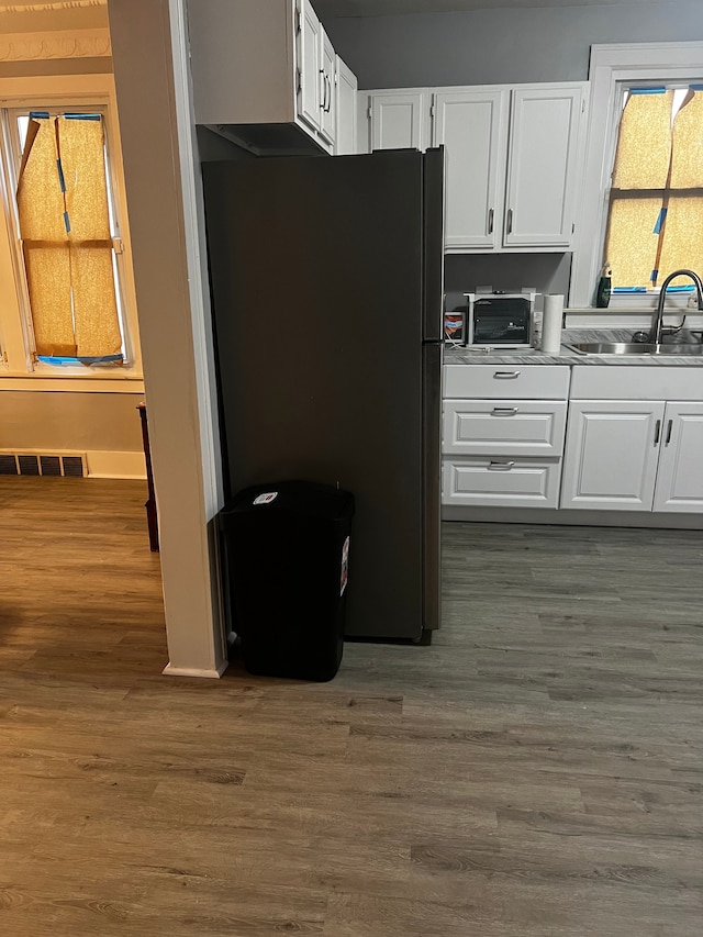 kitchen with dark hardwood / wood-style floors, black refrigerator, white cabinetry, and sink