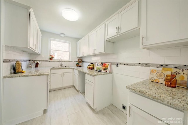 kitchen featuring tasteful backsplash, light stone counters, sink, and white cabinets