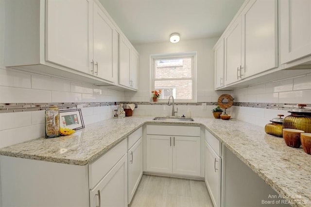 kitchen with light stone countertops, backsplash, white cabinetry, and sink