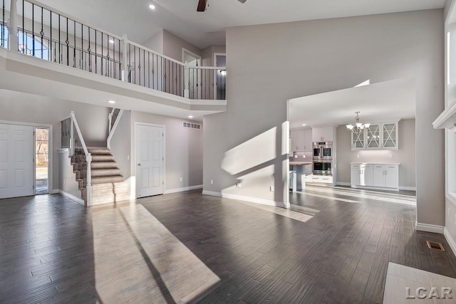 unfurnished living room with ceiling fan with notable chandelier, dark hardwood / wood-style flooring, and a towering ceiling