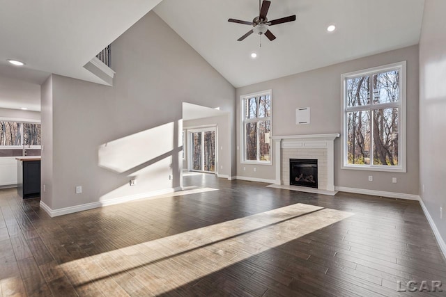 unfurnished living room with dark wood-type flooring, a healthy amount of sunlight, ceiling fan, high vaulted ceiling, and a brick fireplace