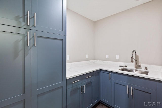 kitchen with light stone counters, sink, and blue cabinets