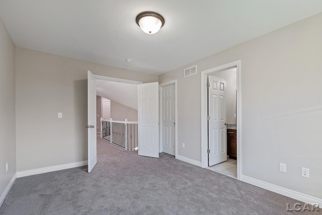 unfurnished bedroom featuring ensuite bath, light carpet, and vaulted ceiling