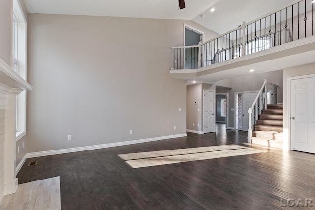 unfurnished living room with ceiling fan, wood-type flooring, a wealth of natural light, and a high ceiling