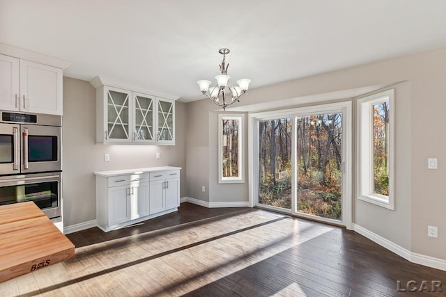 kitchen featuring stainless steel double oven, white cabinets, dark hardwood / wood-style flooring, and an inviting chandelier