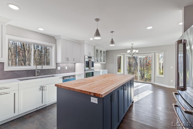 kitchen with pendant lighting, a center island, white cabinetry, sink, and butcher block countertops