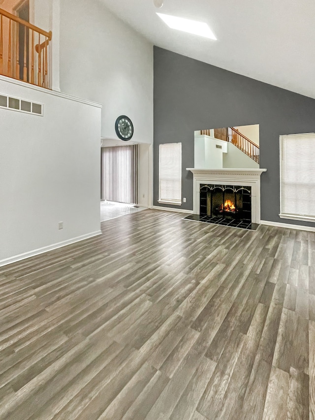 unfurnished living room with a tiled fireplace, wood-type flooring, and high vaulted ceiling