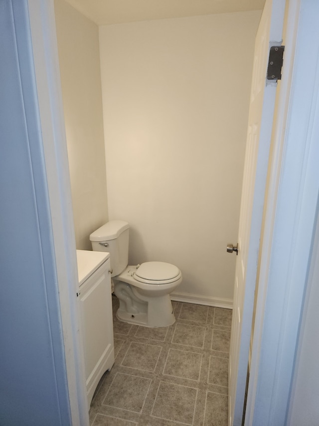 half bath featuring baseboards, vanity, and toilet