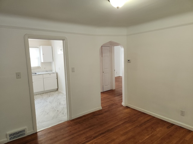 empty room with dark wood-style floors, baseboards, visible vents, and arched walkways