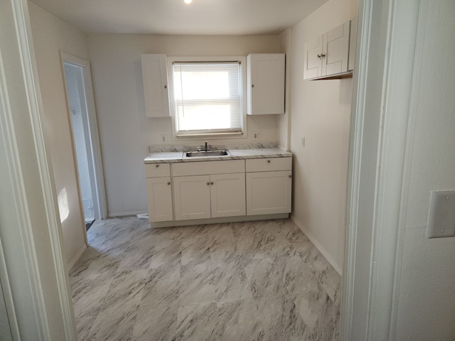 kitchen with marble finish floor, white cabinetry, light countertops, and a sink