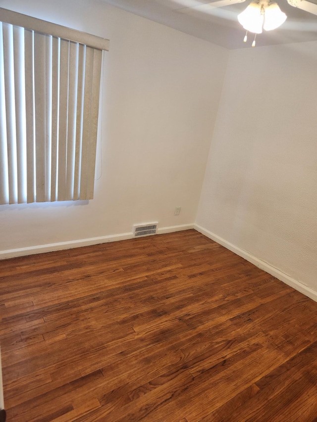 spare room with dark wood-style floors, baseboards, visible vents, and a ceiling fan