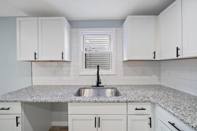 kitchen featuring light stone countertops, backsplash, white cabinetry, and sink