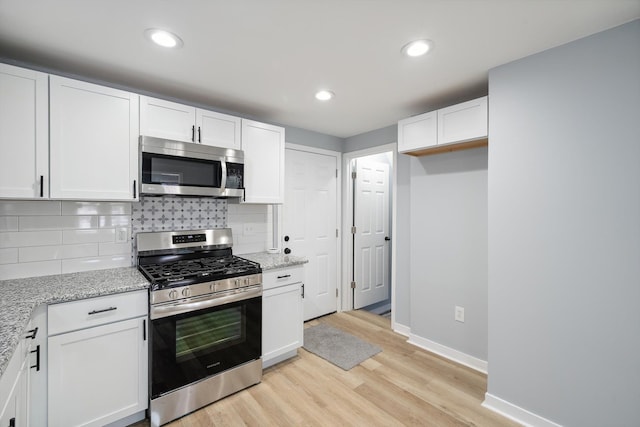 kitchen with decorative backsplash, light stone countertops, stainless steel appliances, light hardwood / wood-style flooring, and white cabinets