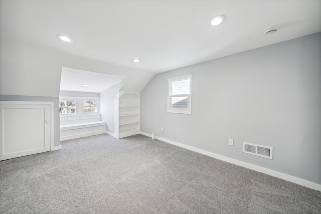 additional living space featuring light carpet, vaulted ceiling, and plenty of natural light