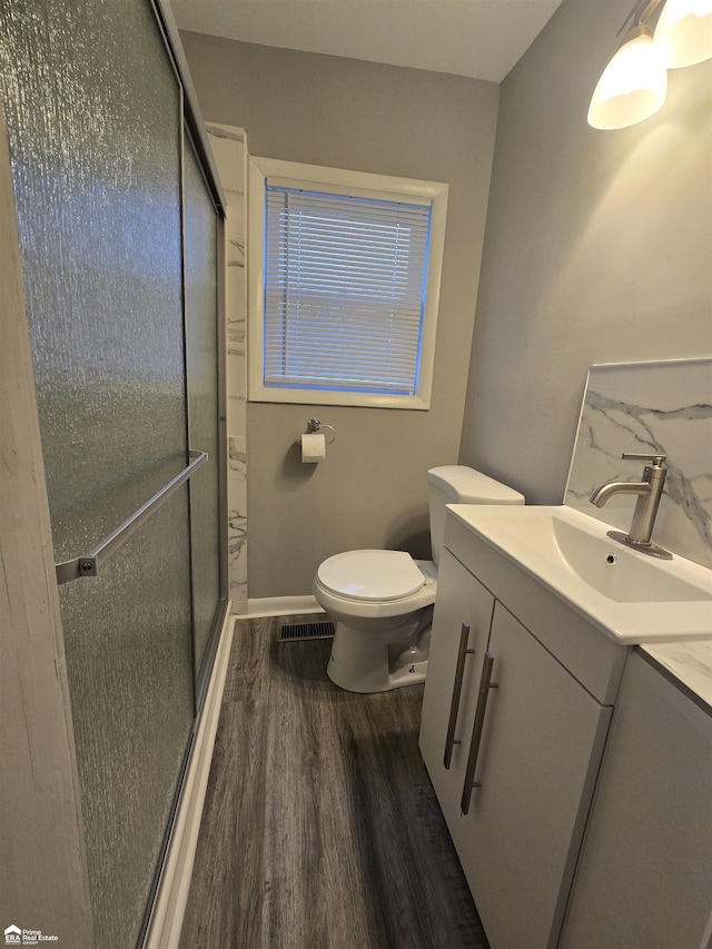 bathroom with hardwood / wood-style floors, vanity, a shower with door, and toilet