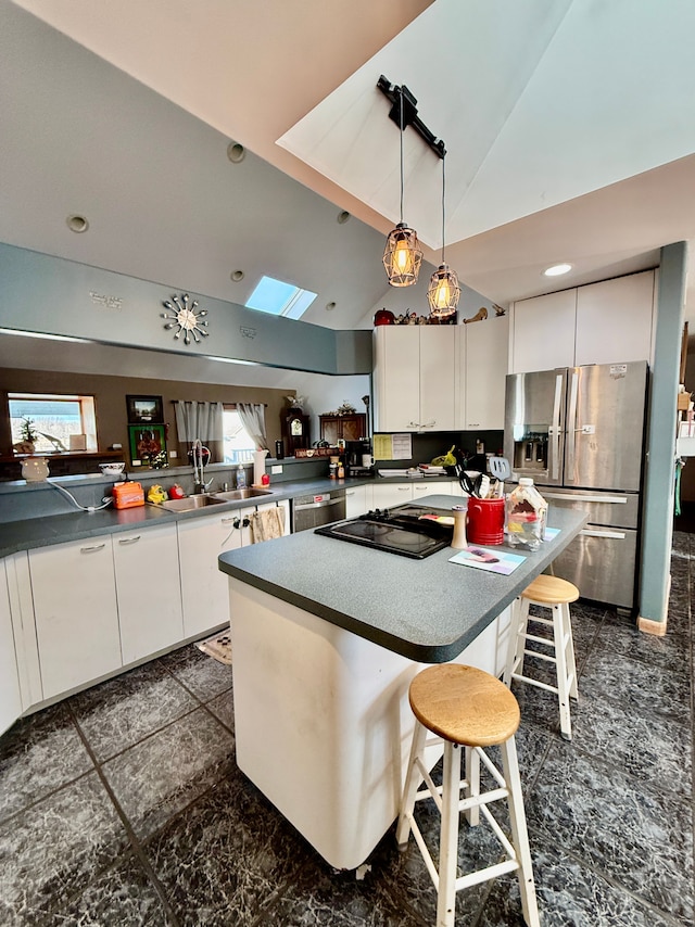 kitchen with vaulted ceiling, appliances with stainless steel finishes, white cabinetry, sink, and a breakfast bar area