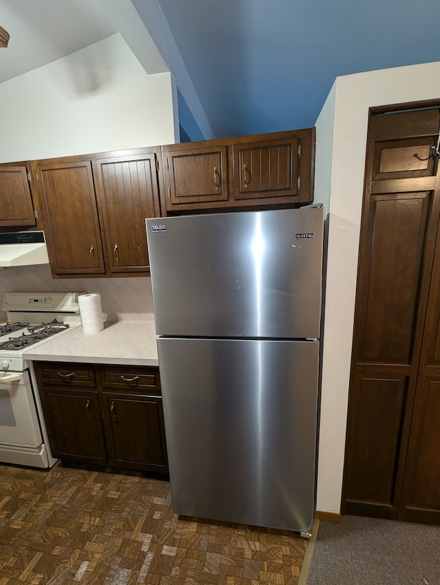 kitchen with dark brown cabinets, ventilation hood, stainless steel refrigerator, and gas range gas stove