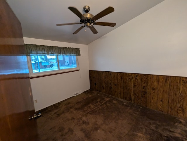 carpeted empty room featuring ceiling fan, wood walls, and vaulted ceiling