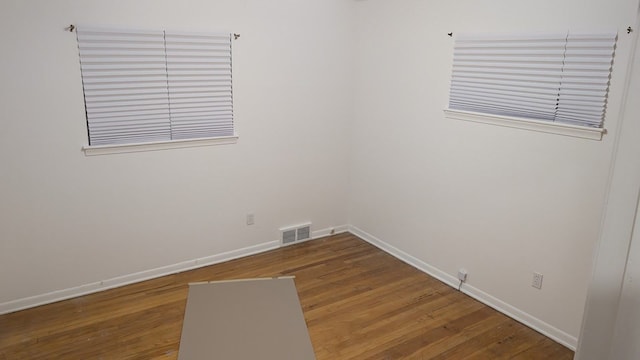 empty room with wood finished floors, visible vents, and baseboards