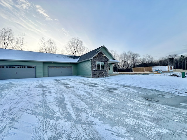 view of snow covered exterior featuring a garage and stone siding