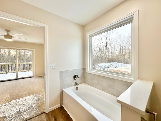 bathroom with a garden tub, a ceiling fan, baseboards, and wood finished floors