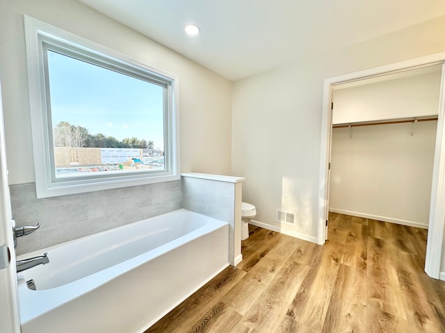 bathroom featuring visible vents, a spacious closet, toilet, wood finished floors, and a bath