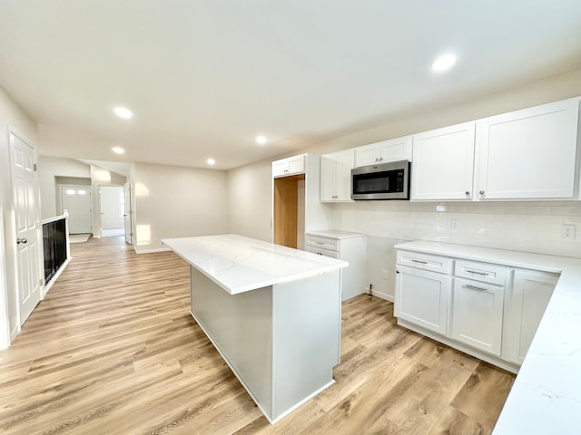 kitchen featuring light wood-type flooring, stainless steel microwave, decorative backsplash, and light stone counters