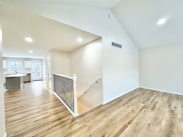 hall featuring lofted ceiling, light wood-style flooring, an upstairs landing, and visible vents