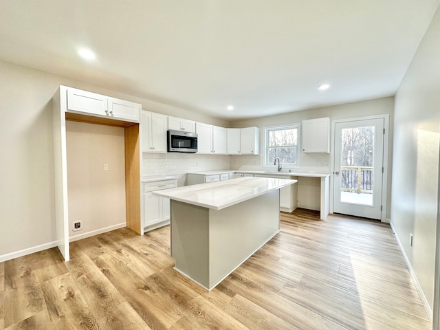 kitchen with white cabinetry, stainless steel microwave, and light wood-style flooring