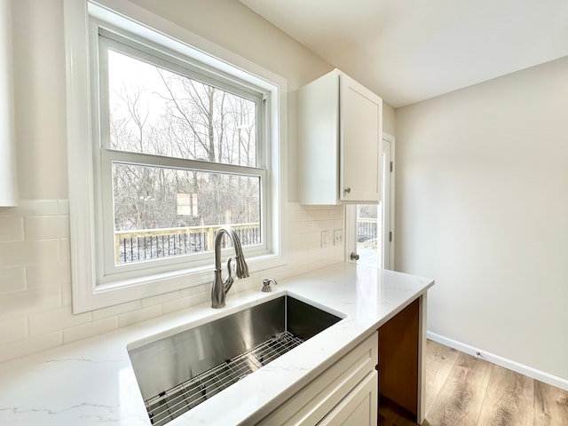 kitchen with light stone counters, wood finished floors, a sink, white cabinetry, and tasteful backsplash