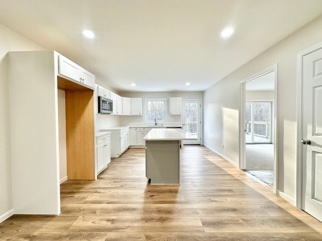 kitchen featuring a sink, white cabinetry, light wood-type flooring, a center island, and stainless steel microwave