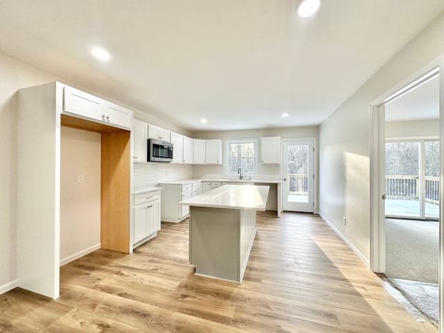 kitchen with white cabinets, light wood-type flooring, backsplash, a center island, and stainless steel microwave