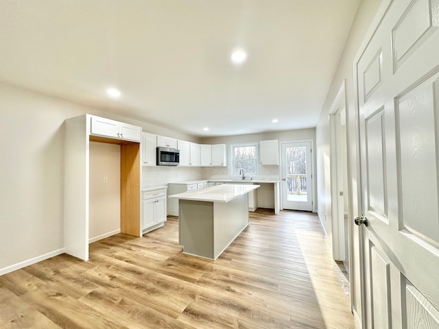 kitchen with stainless steel microwave, light wood-type flooring, white cabinetry, and a center island