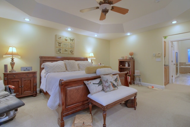 carpeted bedroom with ceiling fan, ensuite bath, and a tray ceiling