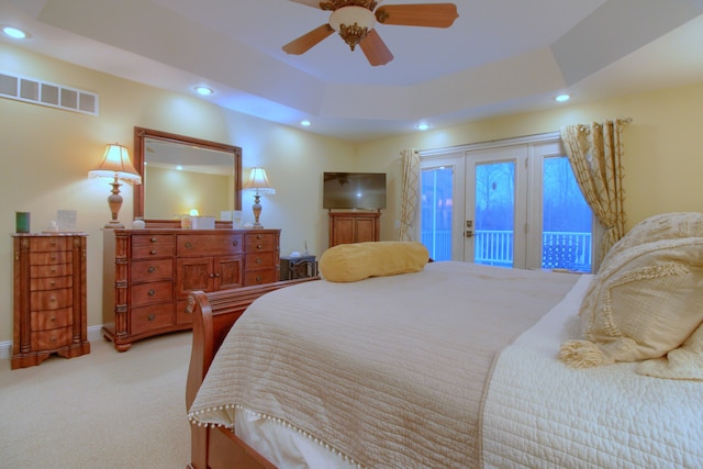 bedroom with ceiling fan, light carpet, access to outside, and a tray ceiling