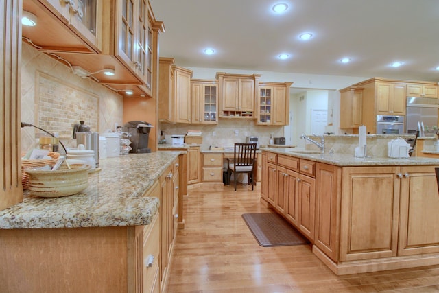 kitchen featuring light stone countertops, light hardwood / wood-style floors, a center island with sink, and sink