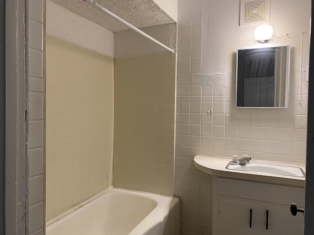 bathroom with tiled shower / bath combo, a textured ceiling, vanity, and tile walls