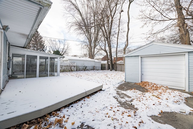 yard layered in snow with a sunroom, an outdoor structure, and a garage