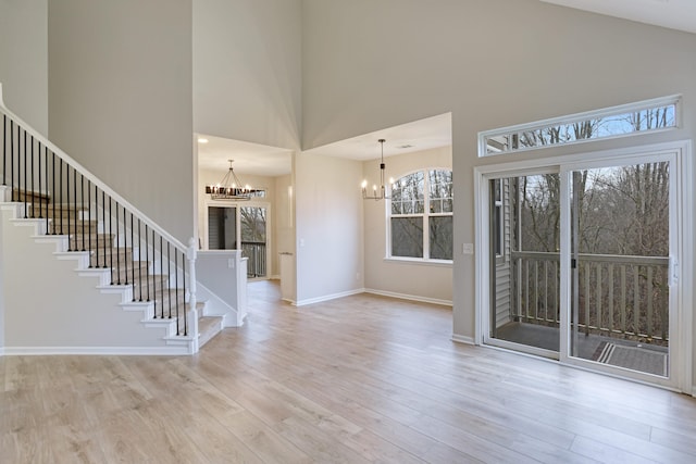 interior space featuring a towering ceiling, light hardwood / wood-style flooring, and an inviting chandelier