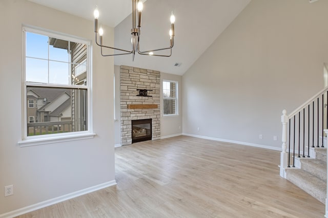 unfurnished living room featuring a stone fireplace, light wood-type flooring, high vaulted ceiling, and an inviting chandelier