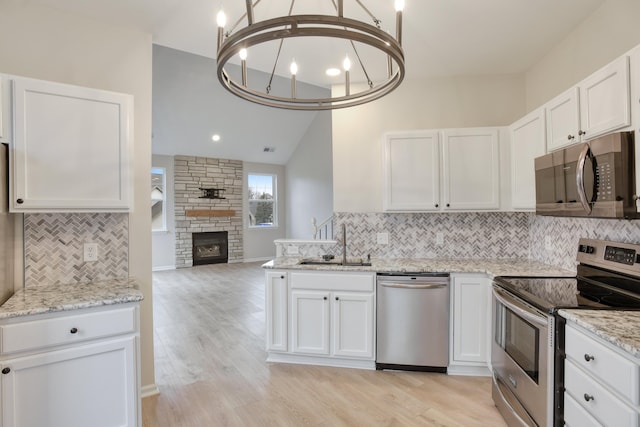 kitchen with appliances with stainless steel finishes, light hardwood / wood-style floors, white cabinetry, and a stone fireplace